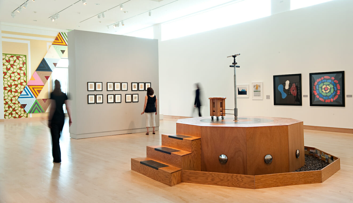 installation view of the 2010 Wisconsin Triennial showing three people inside of the galleries surrounded by sculptures or framed artworks