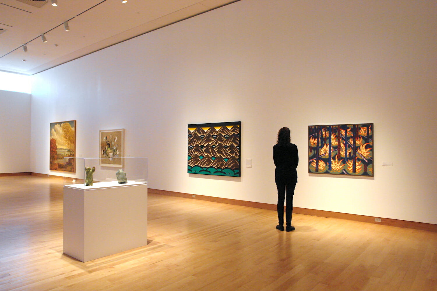 installation view of the exhibition titled Apple Pie featuring a person looking at a painting hanging on a wall, in a room with other paintings on the wall and a vintrine display case