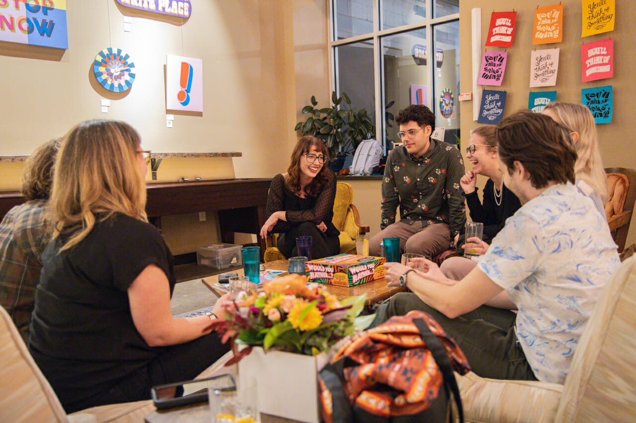 A group of people seated on couches and conversing or laughing with each other during Gallery Night.